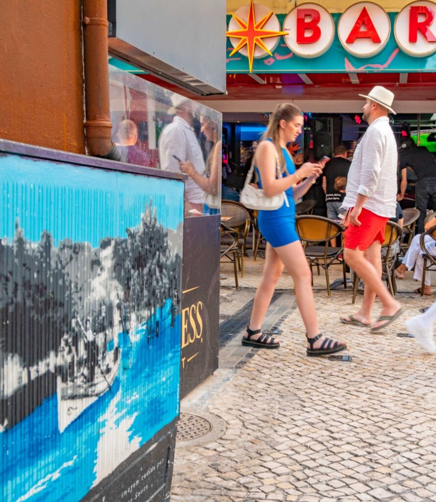 Tourists walk by a Fly Pontes electricity cabinet in Albufeira